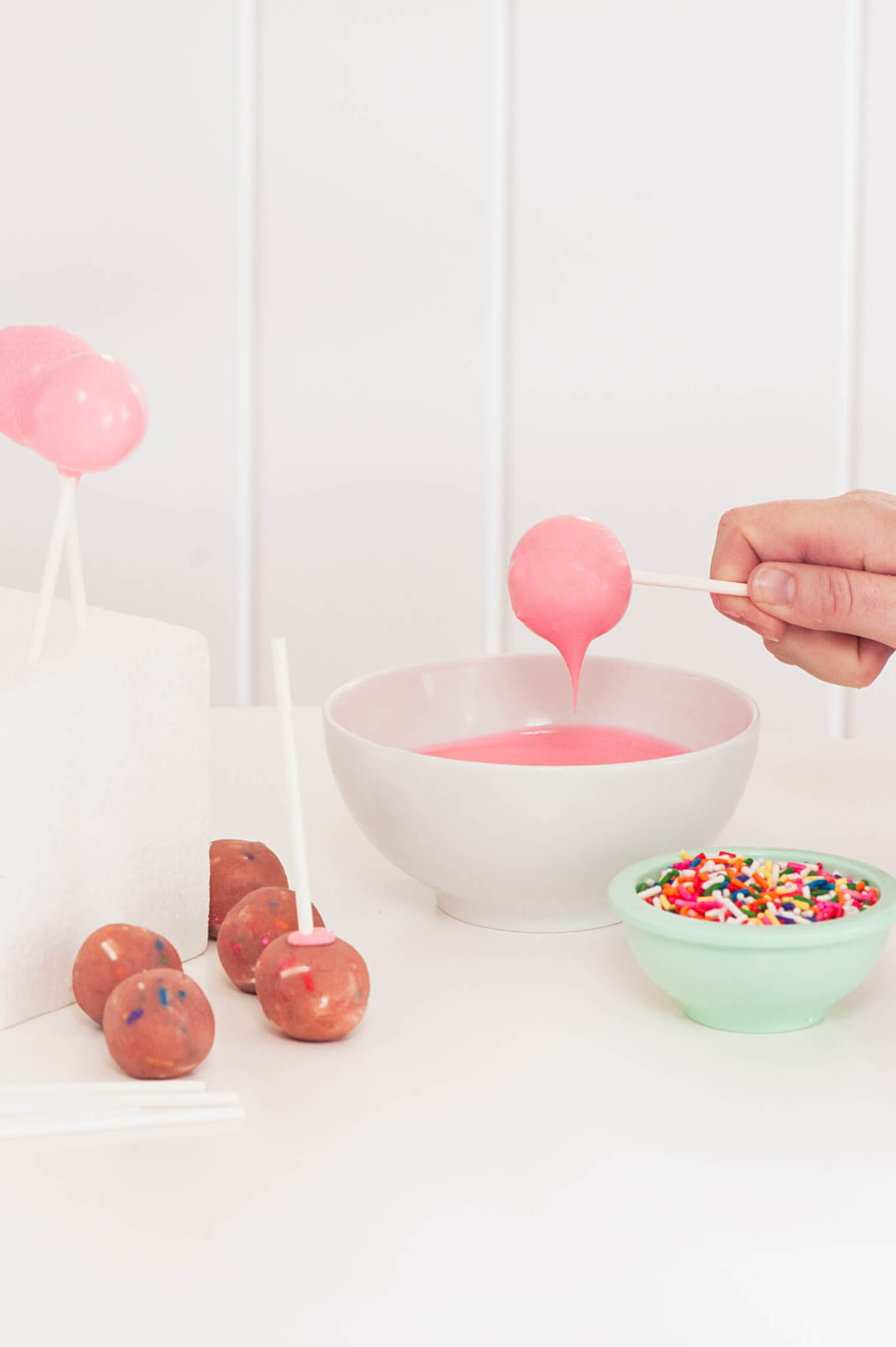 Strawberry Confetti Cake Pops being dipped in pink melting chocolate.